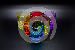 Six multicolored shot glasses placed in triangle on black background