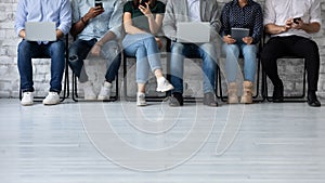 Six multiethnic young people sit in queue holding electronic devices