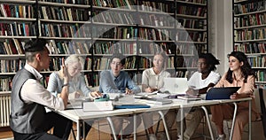 Six multiracial teens students studying seated at table in library