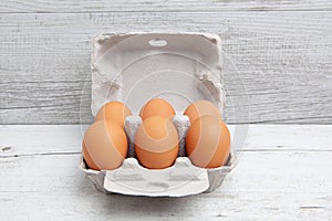 Six pack of eggs in carton on white wooden table.