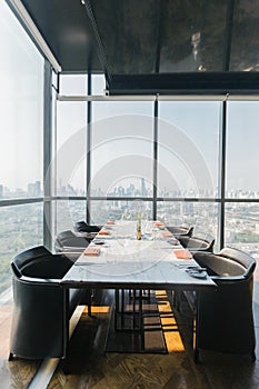 Six people dinner table with plates, knives, forks, wine glasses, glasses and napkins on marble table top with Bangkok cityscape.