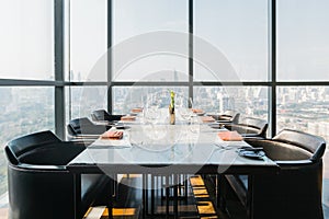 Six people dinner table with plates, knives, forks, wine glasses, glasses and napkins on marble table top with Bangkok cityscape.