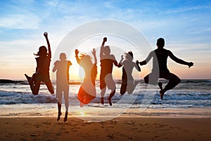 Six people jumping on beach at sunset.