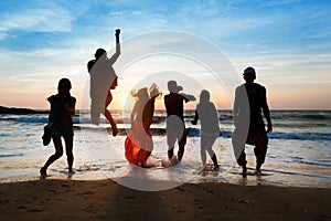 Six people jumping on beach at sunset.