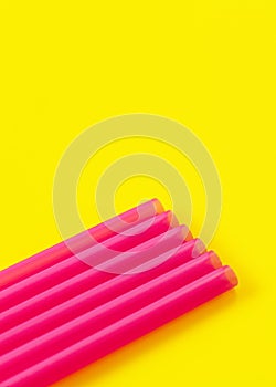 Six pink plastic drinking straws on yellow board, forming diagonal line - abstract closeup detail, space for text above