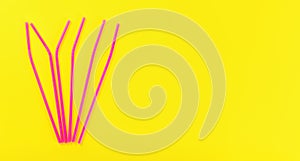 Six pink plastic drinking straws on yellow board, view from above, space for text right side