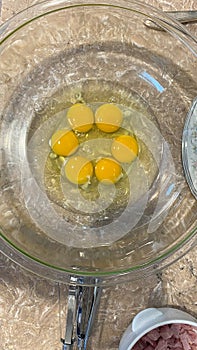 Six raw eggs with unbroken yolk in a clear bowl