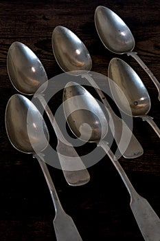 Six silvver spoons lying in a staggered row on wooden table