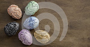 Six unusal embossed carved Art Nouveau style Easter eggs on a dark wooden background.