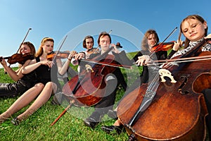 Six violinists sit on grass and play