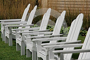 Six white Adirondack chairs on manicured lawn