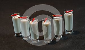 Six white coconut drinks decorated with red peppers, all on a bl
