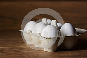 Six white eggs package in a carton on a wooden board