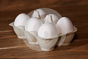 Six white eggs package in a carton on a wooden board