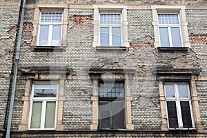 Six white Windows on the facade of the old damaged brick building with a drain pipe