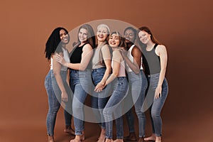 Six women of different ages and body types smiling and laughing over brown background