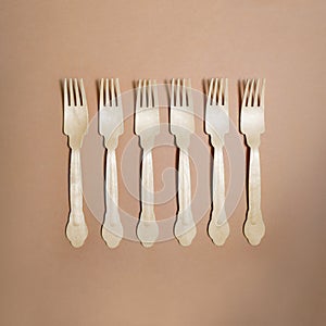 Six wooden plywood forks lay in a line on beige craft background. Zero waste recicle concept. Square template