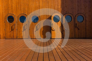 Six wooden ship doors with a porthole on the deck of an old sailing ship for entering passenger cabins. The deck and doors are lig