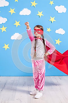 Six year blonde girl dressed like superhero having fun at home. Kid on the background of bright blue wall.