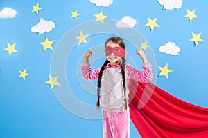 Six year blonde girl dressed like superhero having fun at home. Kid on the background of bright blue wall.