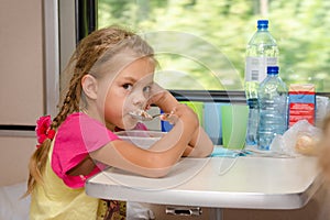 A six-year girl in a train sitting at table on the lower place in the second-class compartment of the car and eats porridge sp