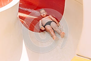 Six-year-old boy in swimming trunks rolling down a water slide in