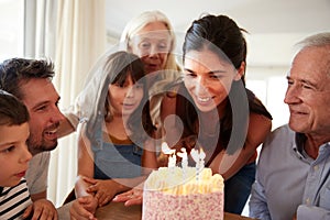 Six year old girl blowing out the candles on birthday cake watched by her mum and family, close up