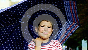 A six-year-old little boy stands outside under an umbrella in the summer.