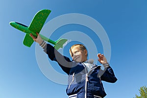 A six-year-old preschooler boy in a blue jacket launches a toy plane in nature against the background of a clear blue sky on a sum