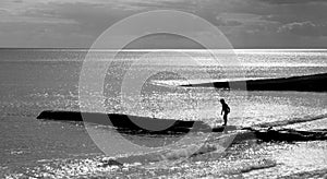 A six year old unrecognisable boy walking along a jetty in the sea, black and white photograph