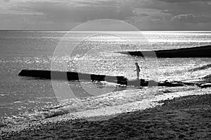 A six year old unrecognisable boy walking along a jetty in the sea, black and white photograph