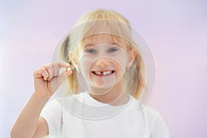 Six year smiling happy girl holding a first fallen tooth and looking at him.