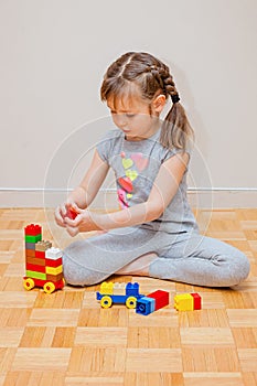 Six years old little girl playing with building blocks toys. Construction activity
