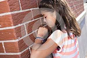 Six years old school girl cry beside brick wall