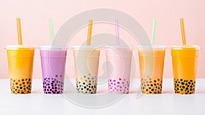 Six yellow and pink bubble tea in transparent plastic cups and straws standing in line on blush pink background