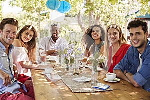 Six young adult friends dining outdoors smiling to camera