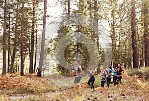 Six young adults running in a row through a forest