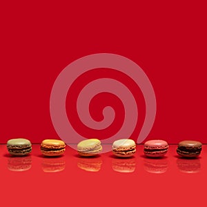 Sixt different color and taste macarons in a horizontal line against a smooth red background. Creative copy space above
