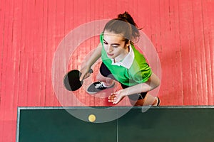 Sixteen-year-old teen girl makes a serve of the ball in table tennis, top view. Teens and ping pong