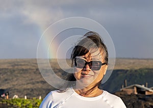 Sixty-three year-old female Korean tourist standing with a rainbow in the background in Hawaii Volcanoes National Park.