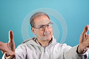 A sixty-year-old baby boomer in a casual grey hoodie with facial stubble is looking at the camera with arms outstretched