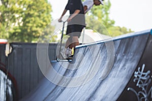 Skate park view with kids on a kick scooter doing tricks and stunts, boys in a skate park riding bmx bike and skate, playing and