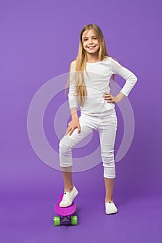Skateboard kid in casual wear on violet background. Girl skater smiling with longboard. Small child smile with skate