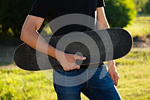 Skateboard longboard close-up in the hands of a young man in jeans and a black T-shirt in the park