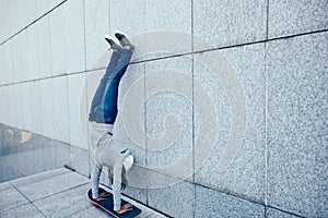 Skateboarder doing a handstand on skateboard against wall