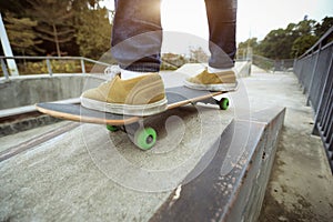 Skateboarder legs riding skateboard at skatepark ramp