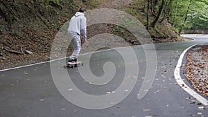 Skateboarder riding carving turns on skateboard on winding road mountain forest