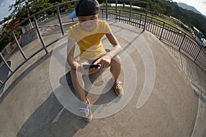 Skateboarder sit on skateboard use mobile phone