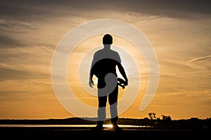 Skater standing on road and holding a skateboard against the sunset