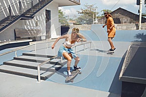 Skateboarding. Couple Riding On Skateboards At Skatepark. Skaters In Casual Outfit Doing Tricks On Concrete Ramp